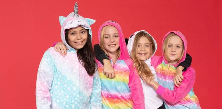 Girls wearing unicorn onesies on red background