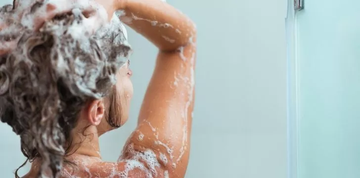 A woman using shampoo in her hair in the shower