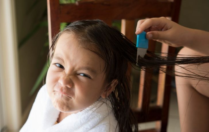 A girl scrunching up her face as her mother checks her hair for head lice with a comb