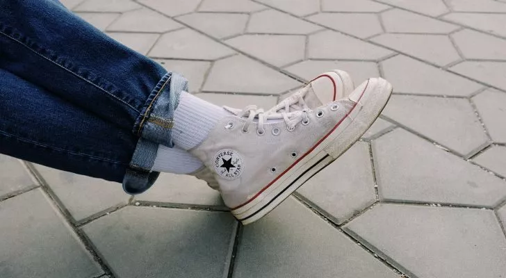 Crossed legs wearing white Chuck Taylor Converse shoes